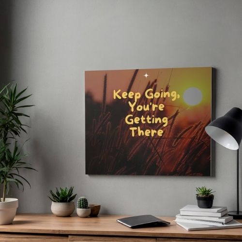 Decorative wall art with motivational quote on a wall above a desk with plants and books.