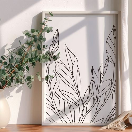 Framed line art of leaves on a white wall with a plant to the left