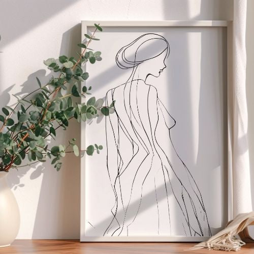 Framed line art of a woman's silhouette on a white wall with a plant to the left.