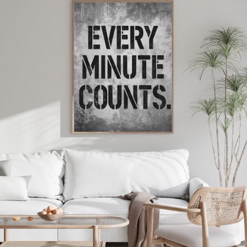 Living room with a white sofa, wicker chair, and framed poster with 'Every Minute Counts' text.